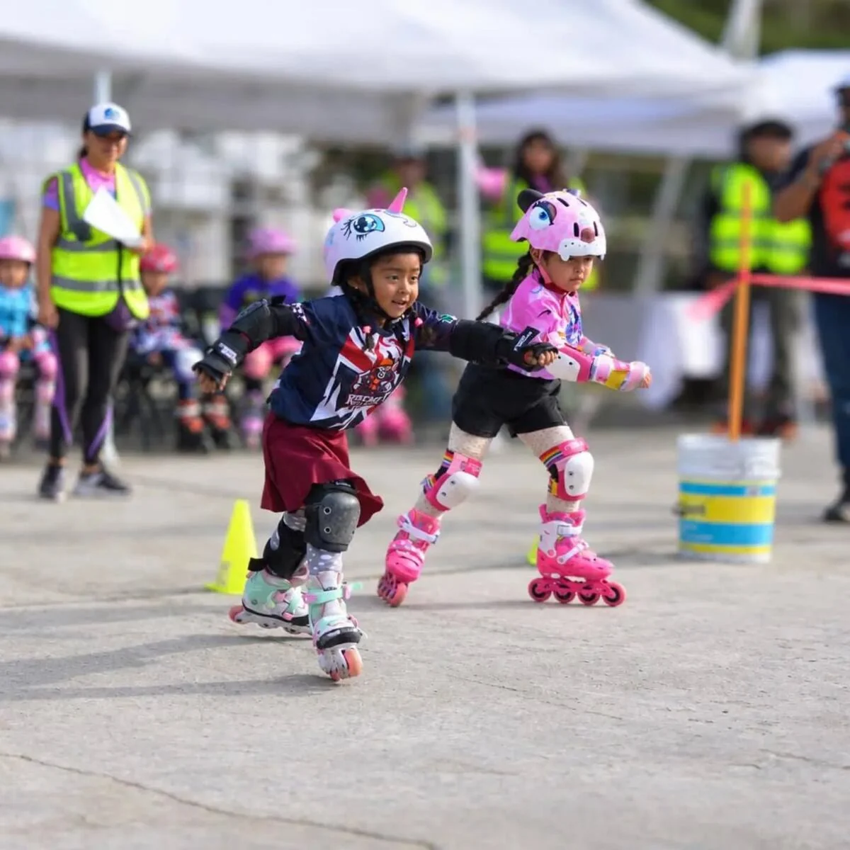 Dos niñas patinan con casco y protecciones en un encuentro deportivo.